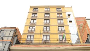 Un edificio de varios pisos con balcones, una bandera visible y un cielo despejado.