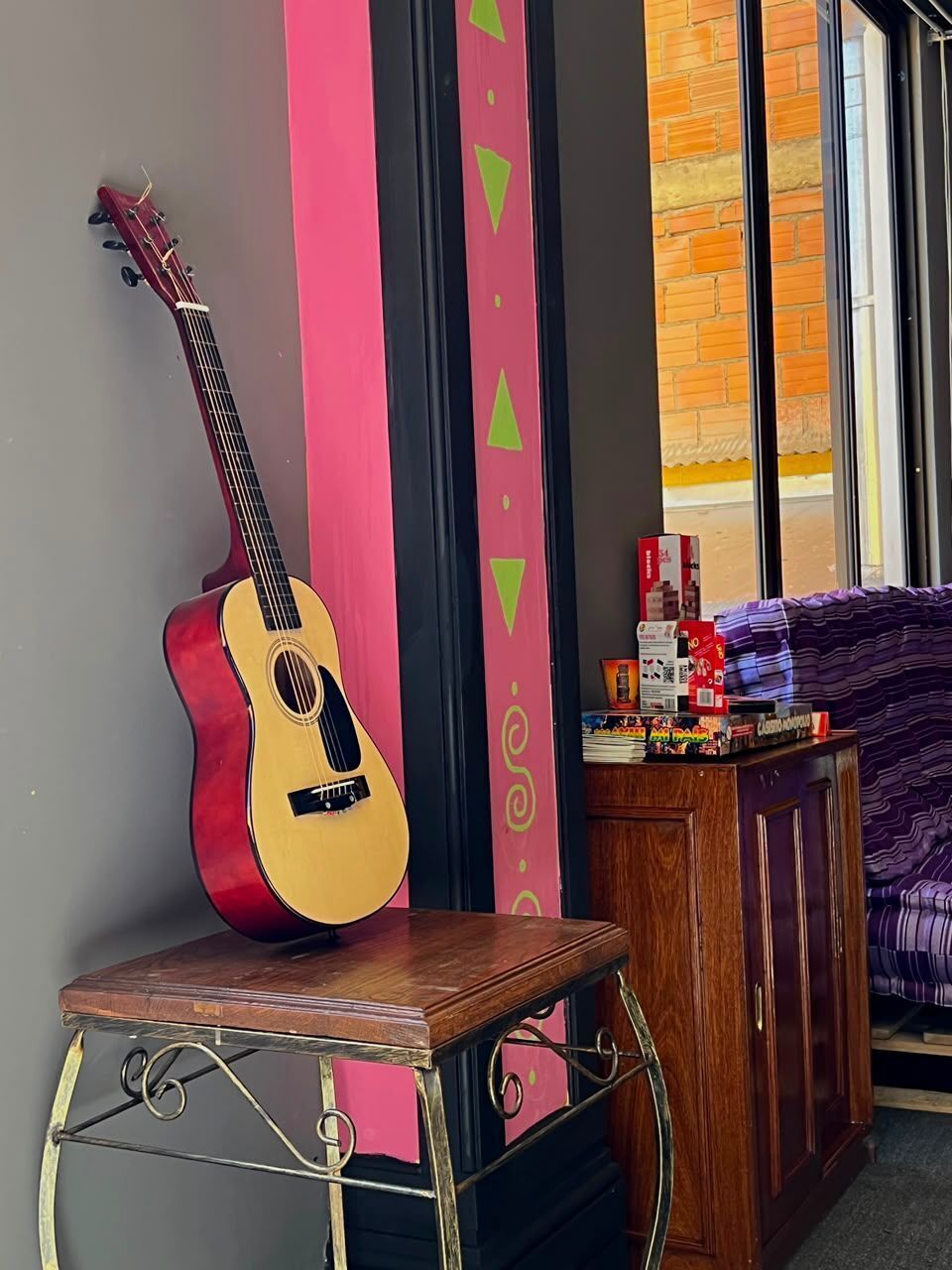 A room with a guitar leaning against a wall, a small table, and a window with a view.