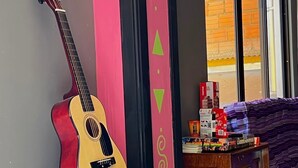 Una habitación con una guitarra apoyada en una pared, una mesita y una ventana con vistas.