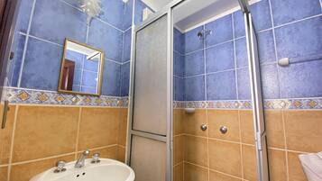 Casa de banho com azulejos azul e bege, uma sanita branca e um cabine de duche de vidro.