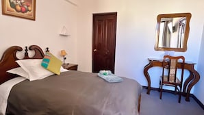 Un dormitorio con una cama de madera, un escritorio con una silla, un espejo y un cuadro en la pared.
