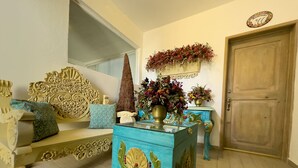 Ein Zimmer mit Holztür, einem blauen Schminktisch mit floralem Dekor, einer Couch mit Zierkissen und einem an der Wand befestigten Spiegel.