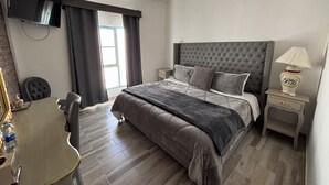 Ein modernes Schlafzimmer mit einem gesteppten Bett, einem Nachttisch mit Lampe, einem Schreibtisch mit Stuhl und einem an der Wand befestigten Flachbildfernseher.