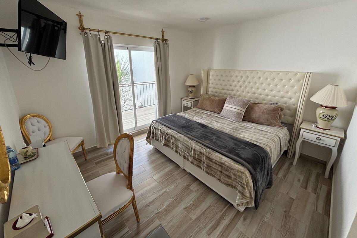 A bedroom with a bed, bedside tables, a chair, a TV, and a balcony view.