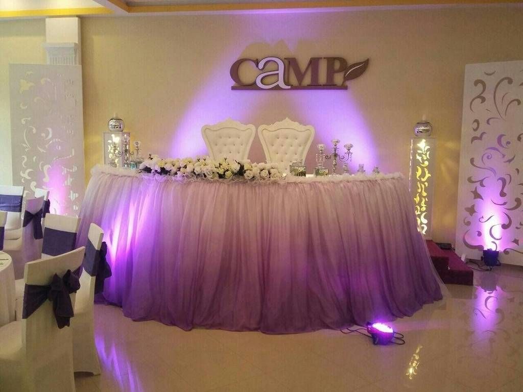 A reception area with a purple draped table, white chairs, and a 'CAMP' sign on the wall.