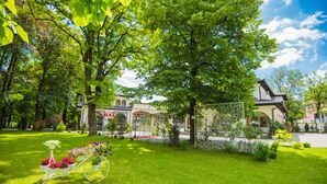A lush garden with a white bicycle, a building with a sign reading "BAI", and a clear blue sky. - Hotel Camp Karagaq (Pec)