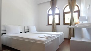 A hotel room with two single beds, a bedside table with a lamp, and a window with curtains. - Hotel Camp Karagaq (Pec)
