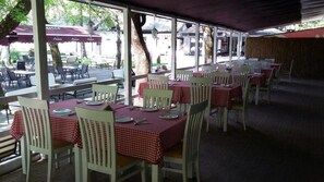 An outdoor dining area with tables and chairs, covered by a roof, and surrounded by trees. - Hotel Camp Karagaq (Pec)
