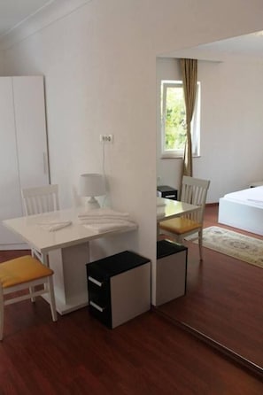 A compact hotel room with a small dining table, two chairs, a lamp, a bed, and a mirror. - Hotel Camp Karagaq (Pec)