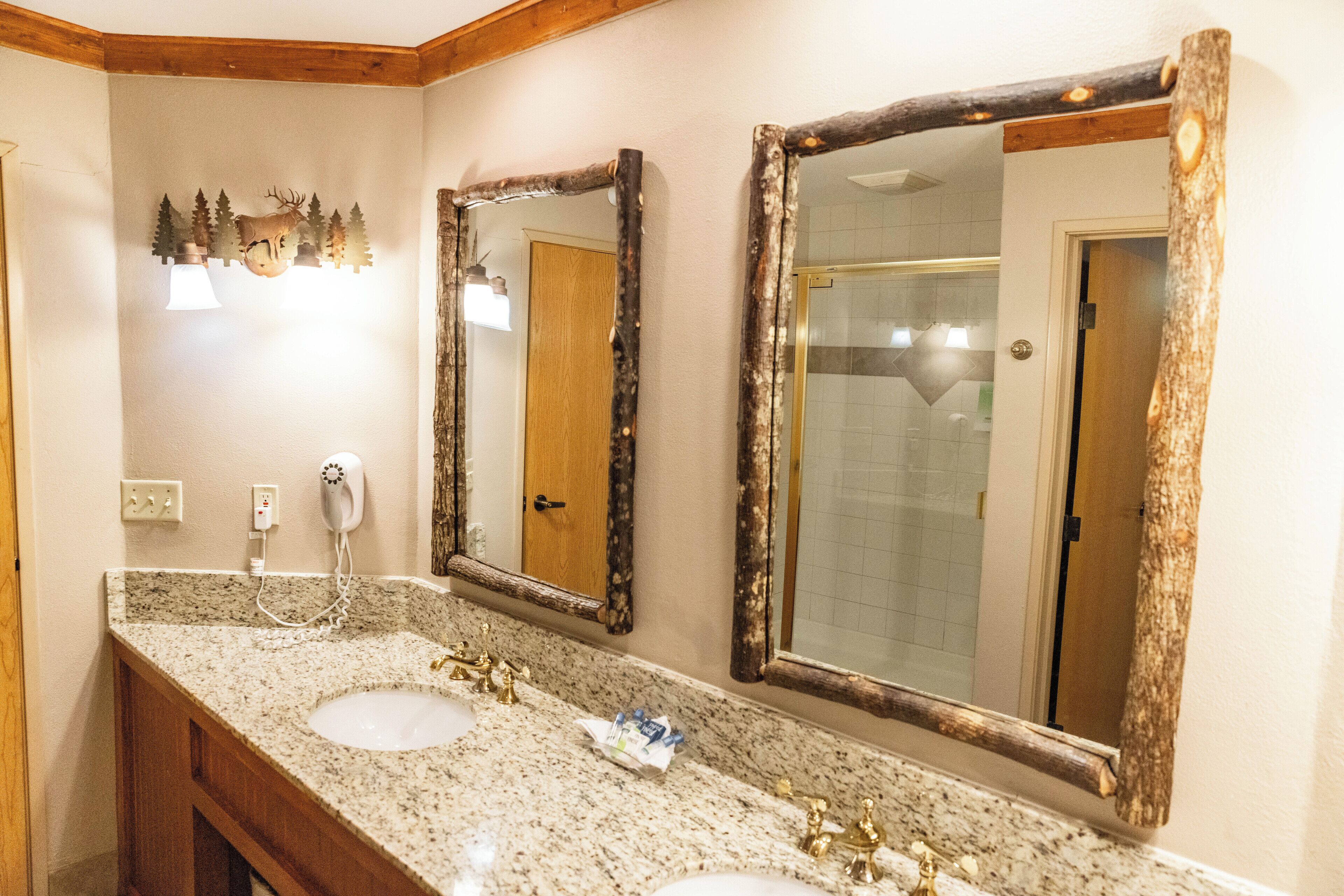 A bathroom with two sinks, wooden vanity, and large mirrors with rustic frames.