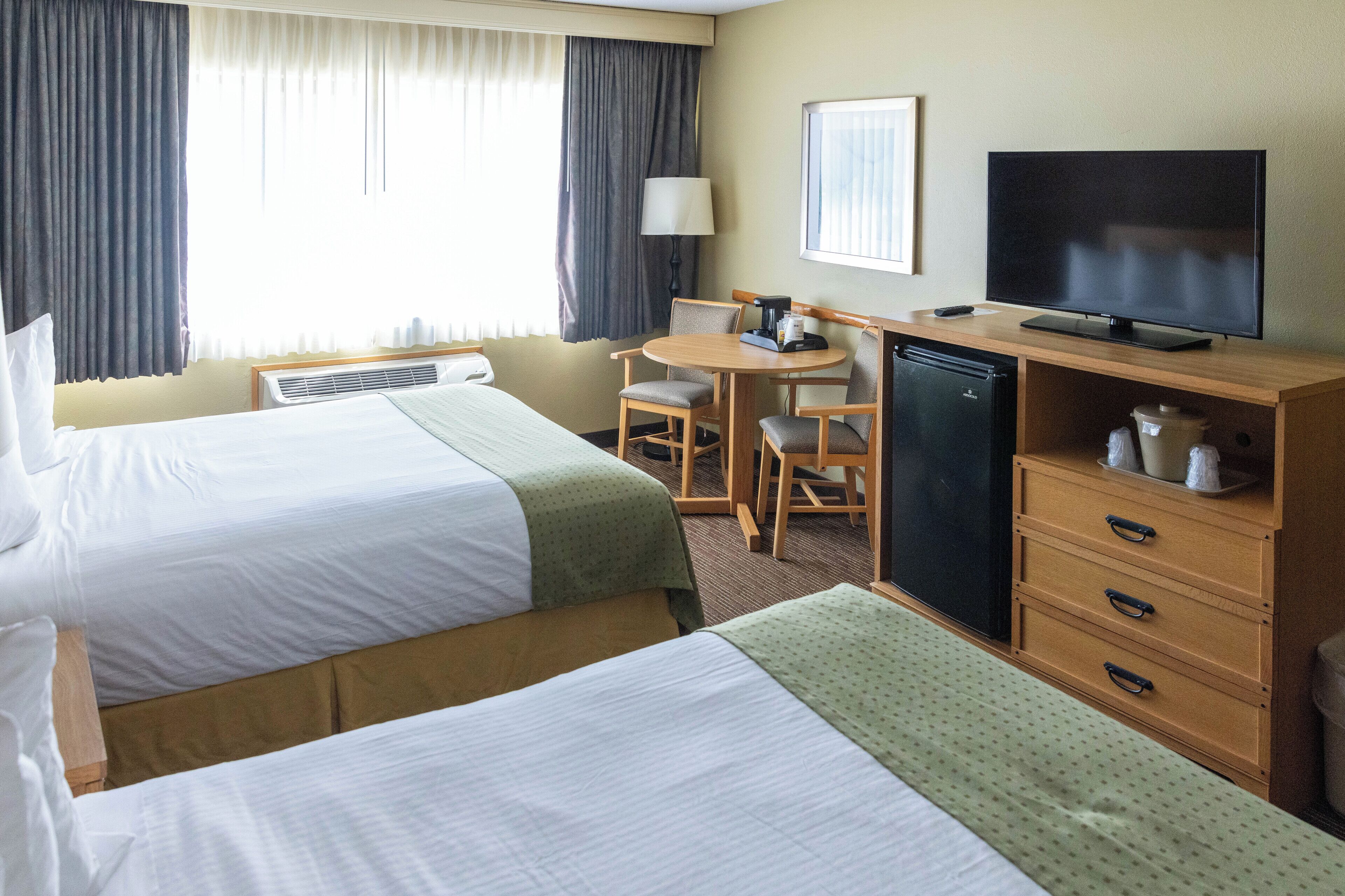 A hotel room with two beds, a desk with a television, a lamp, and a small refrigerator.