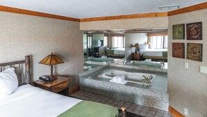 Una habitación de hotel con una cama, una mesita de noche con lámpara, un espejo grande, un baño con bañera y lavamanos, y obras de arte en la pared.