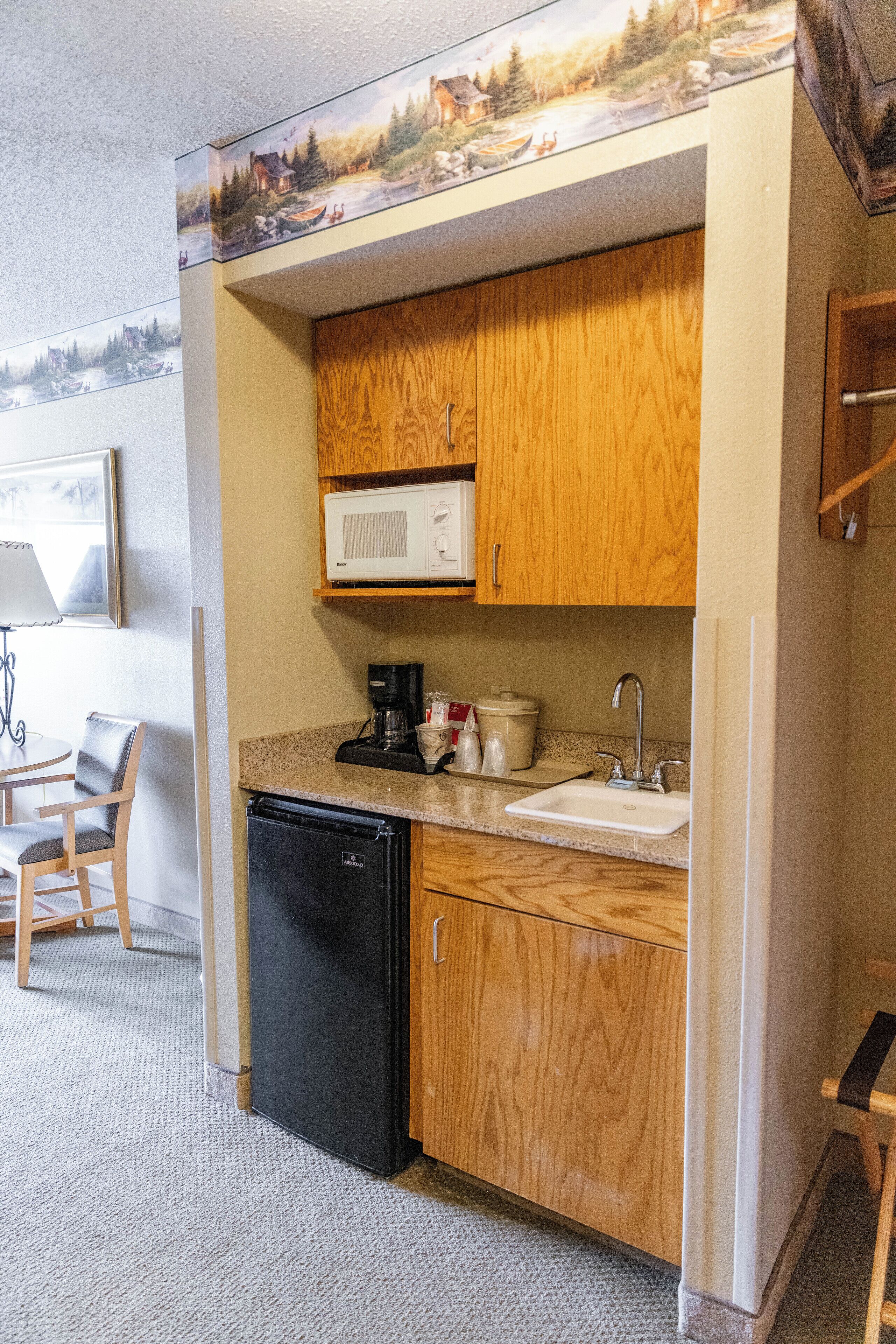 A compact kitchen with wooden cabinets, a microwave, a sink, a coffee maker, and a compact refrigerator.