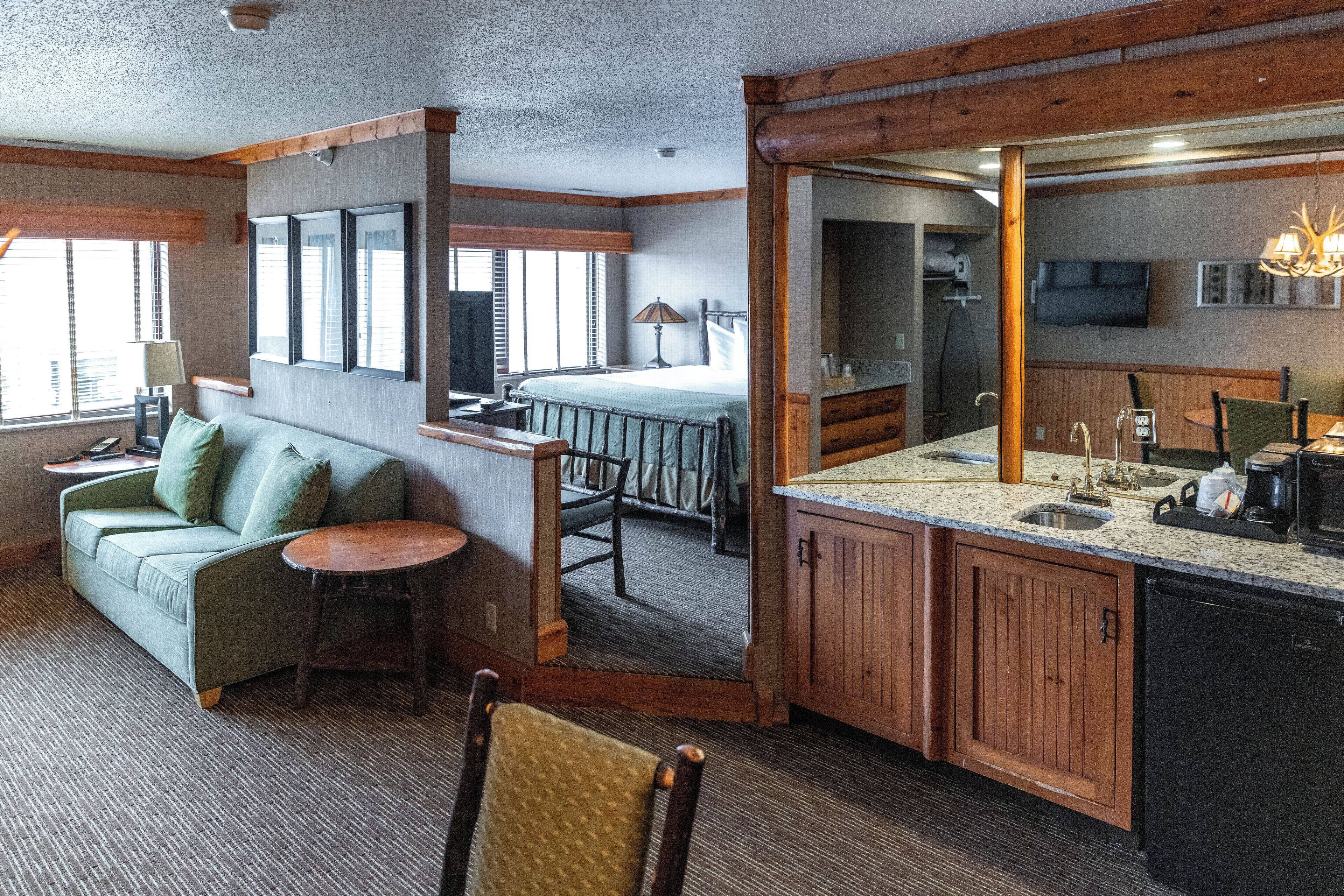 A compact hotel room with a kitchenette, a sofa, a dining table, and a bed.