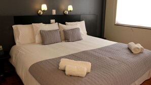 Un lit bien fait, avec du linge de lit blanc et gris, un plaid gris et des serviettes pliées posées sur le lit.