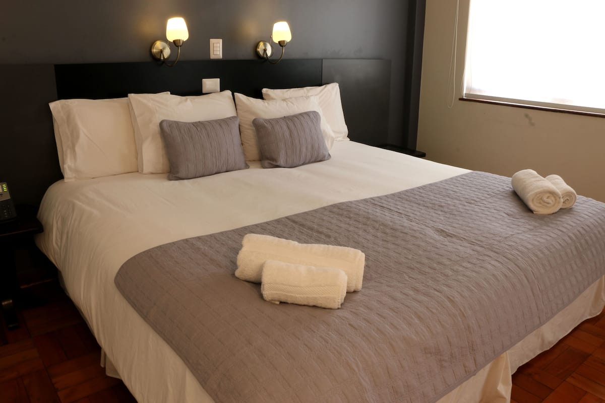 Un lit bien fait, avec du linge de lit blanc et gris, un plaid gris et des serviettes pliées posées sur le lit.