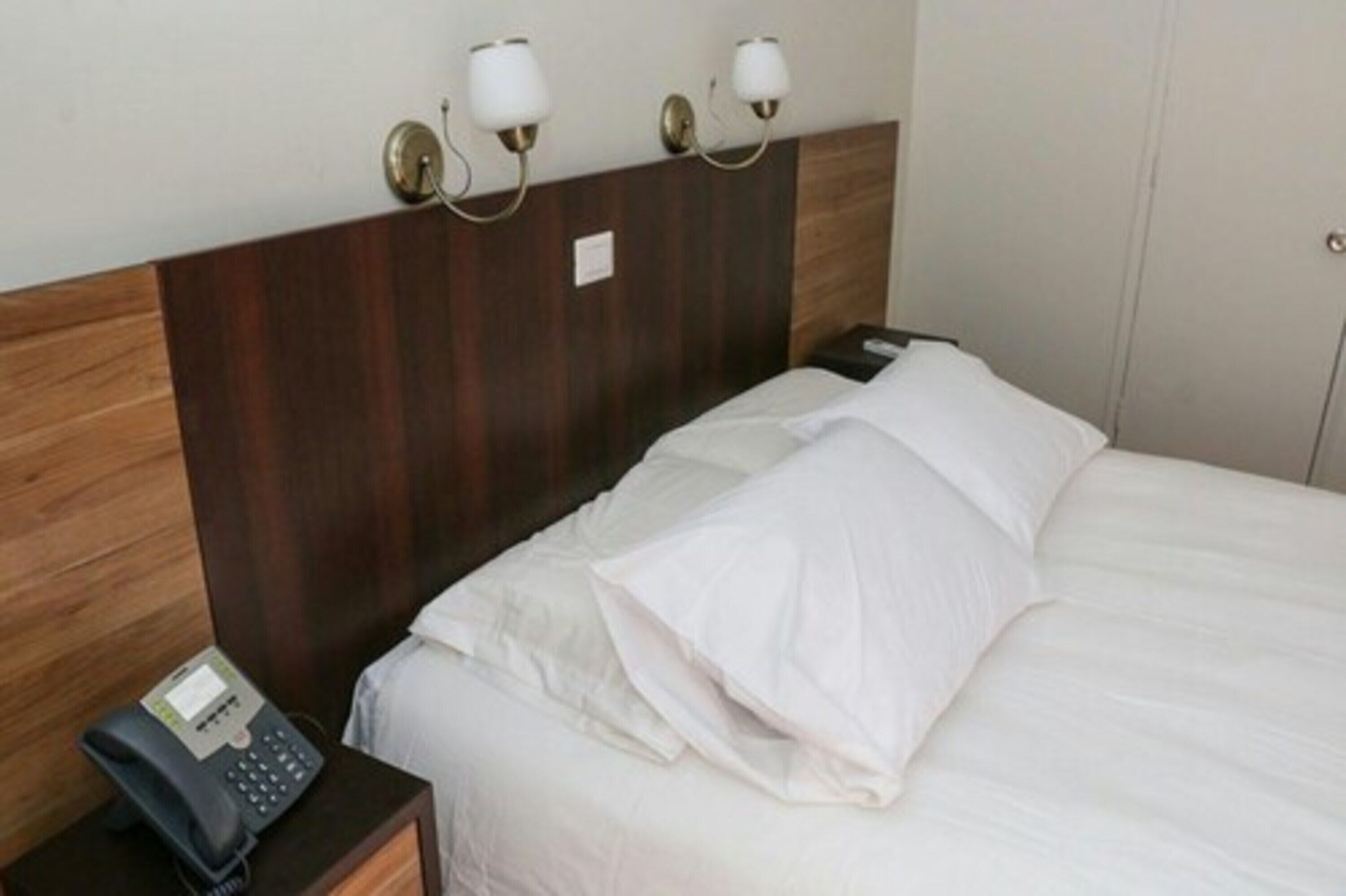 Ein Hotelzimmer mit einem hölzernen Kopfteil, einem Bett mit weißer Bettwäsche und einem Nachttischtelefon.