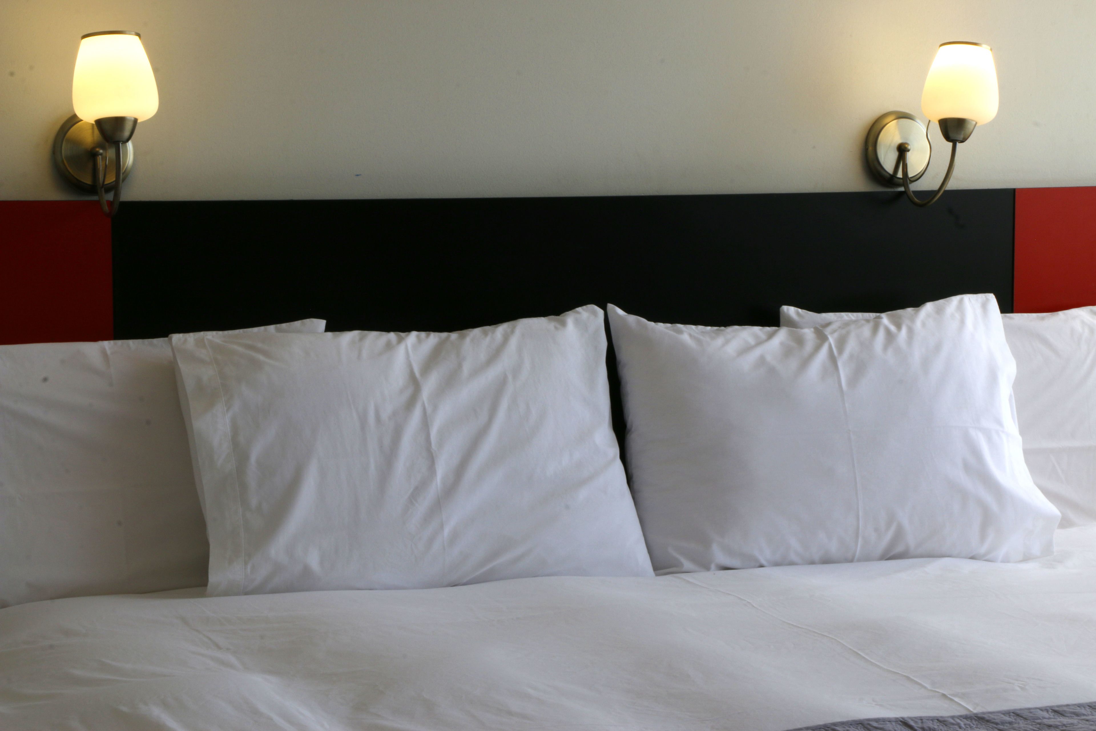 A bed with white bedding and two wall-mounted lamps.