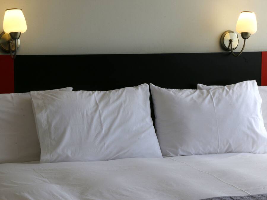 A bed with white bedding and two wall-mounted lamps.
