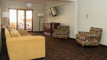 A room with a yellow sofa, two floral armchairs, a wooden cabinet, and a TV mounted on the wall.
