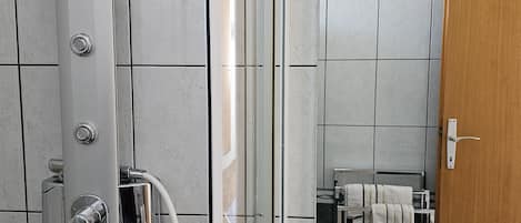 A modern bathroom with a glass-enclosed shower, a white sink, and a wooden door.