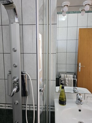 A modern bathroom with a glass-enclosed shower, a white sink, and a wooden door. - Adria Apartments (Dubrovnik)