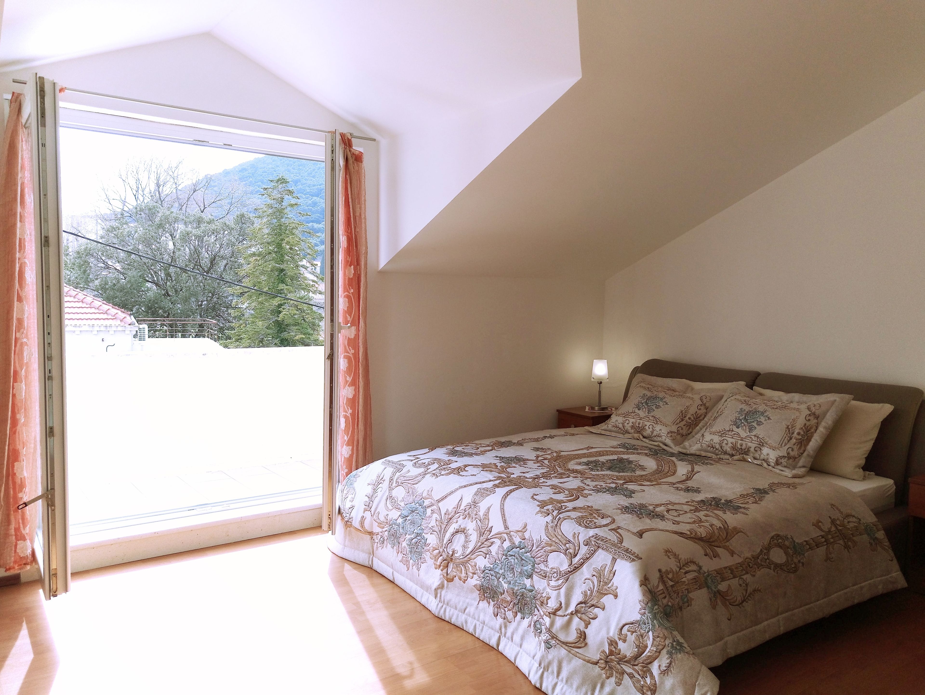 A bedroom with a large bed, a nightstand, and a window with curtains.