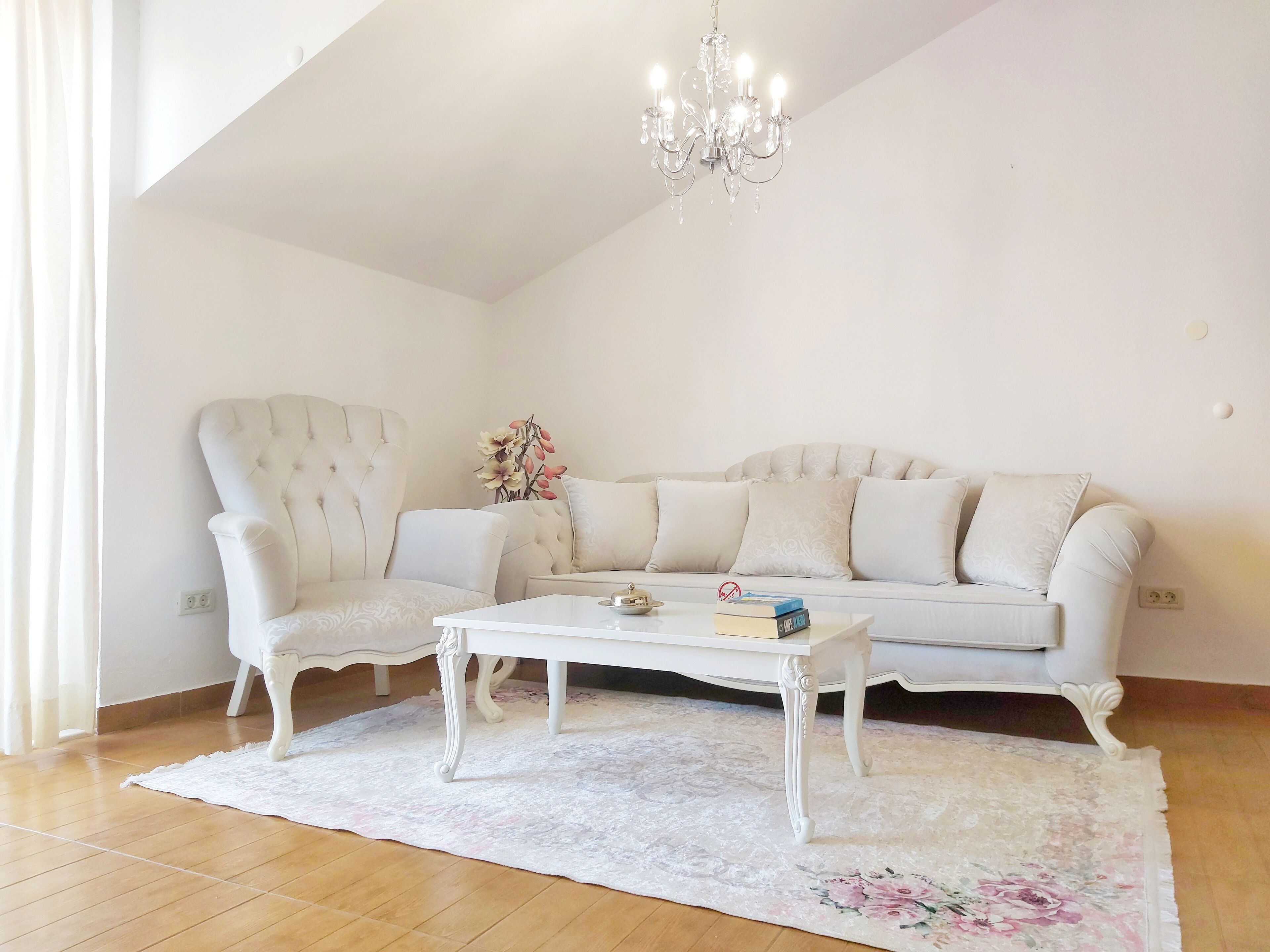 Un salon avec un canapé blanc, un fauteuil assorti, une table basse blanche et un lustre.