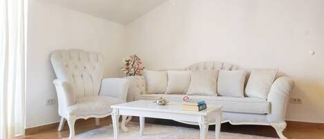 Un salon avec un canapé blanc, un fauteuil assorti, une table basse blanche et un lustre.