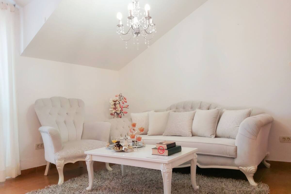 A living room with a white sofa, a white armchair, a white coffee table, and a chandelier.