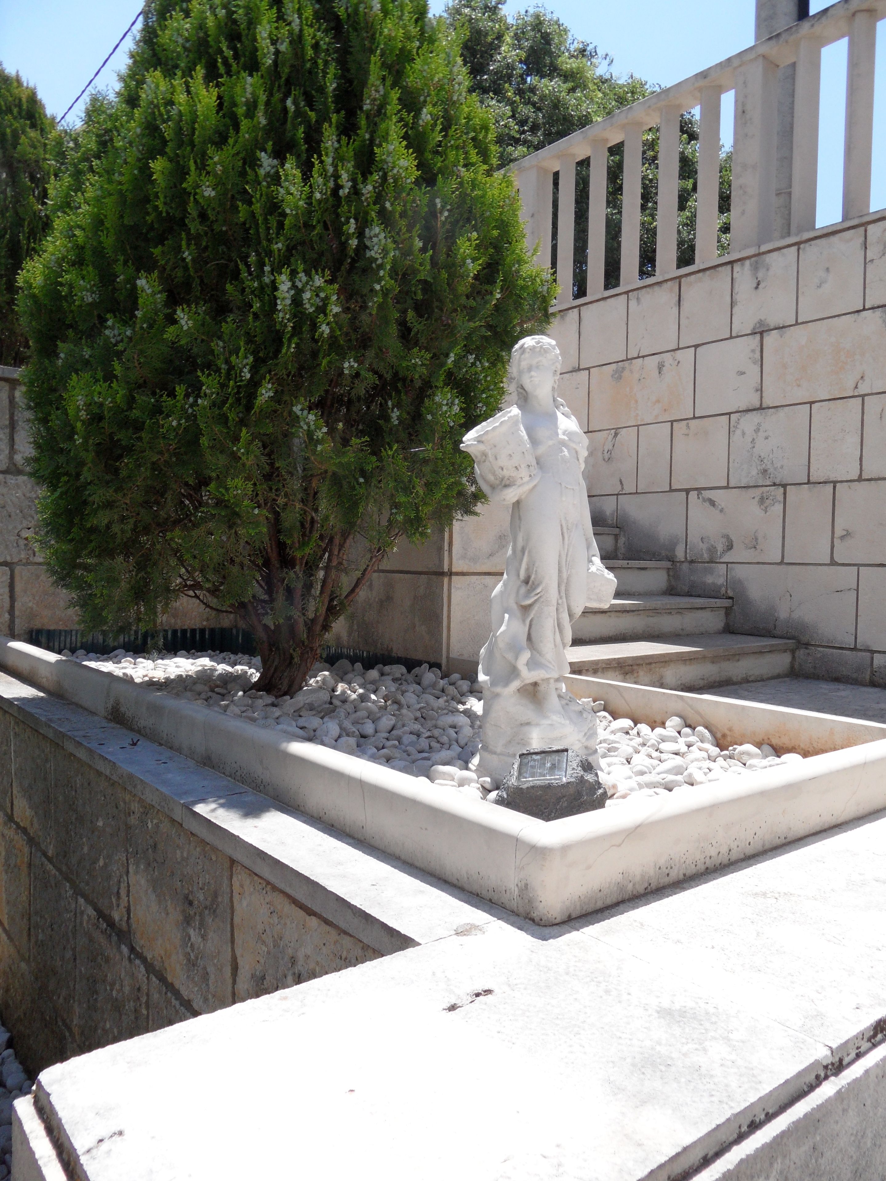 A statue in a garden with a stone wall and a tree.