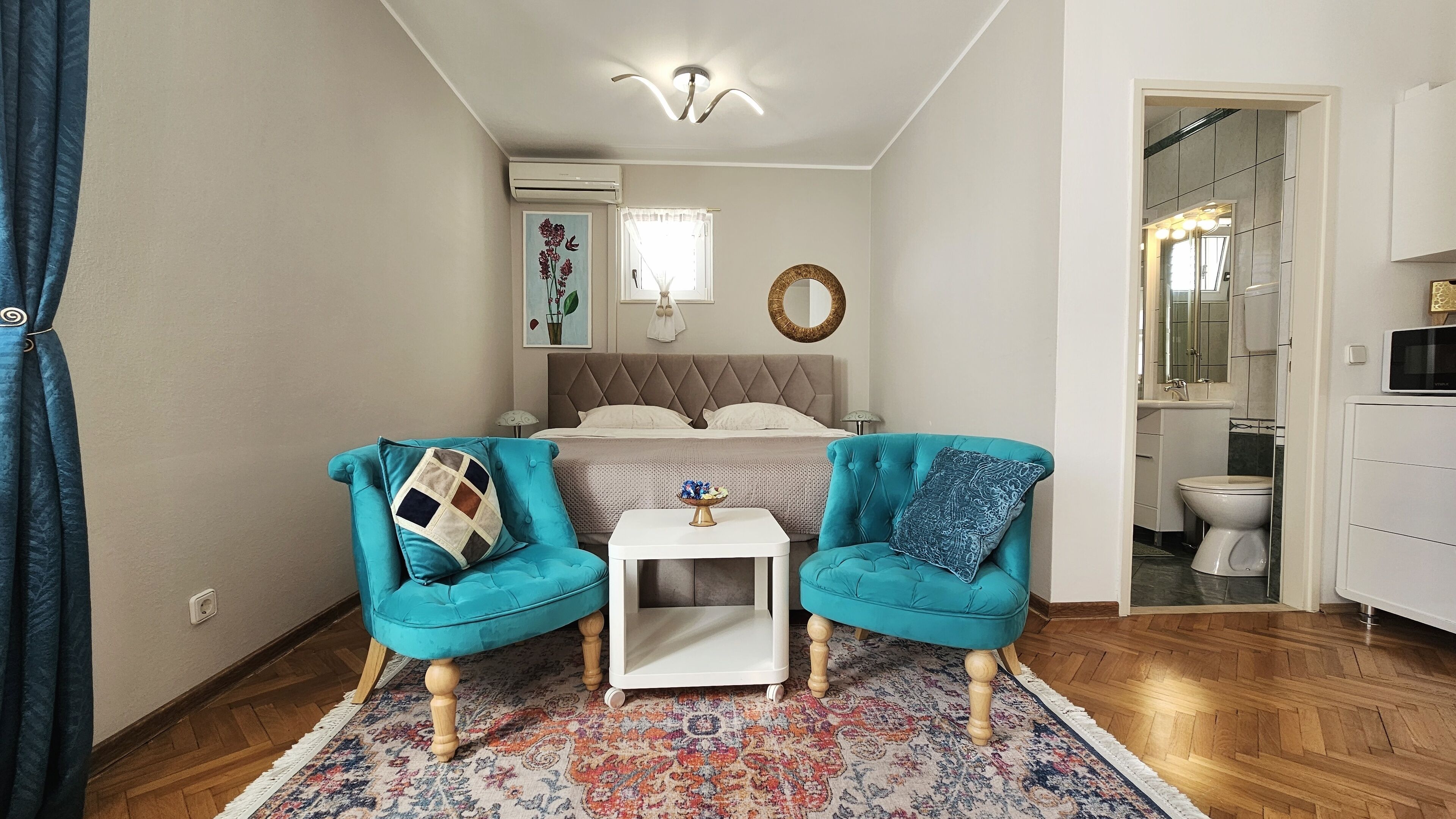 Una camera da letto moderna con un letto, due poltrone color acquamarina, un tavolino bianco e un tappeto decorato.