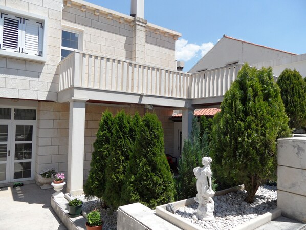 A building with a balcony, potted plants, and a statue in the courtyard. - Adria Apartments (Dubrovnik)