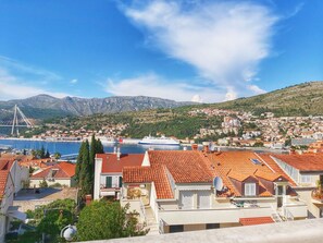 A coastal town with terracotta-roofed buildings, a marina, and a cable-stayed bridge in the background. - Adria Apartments (Dubrovnik)