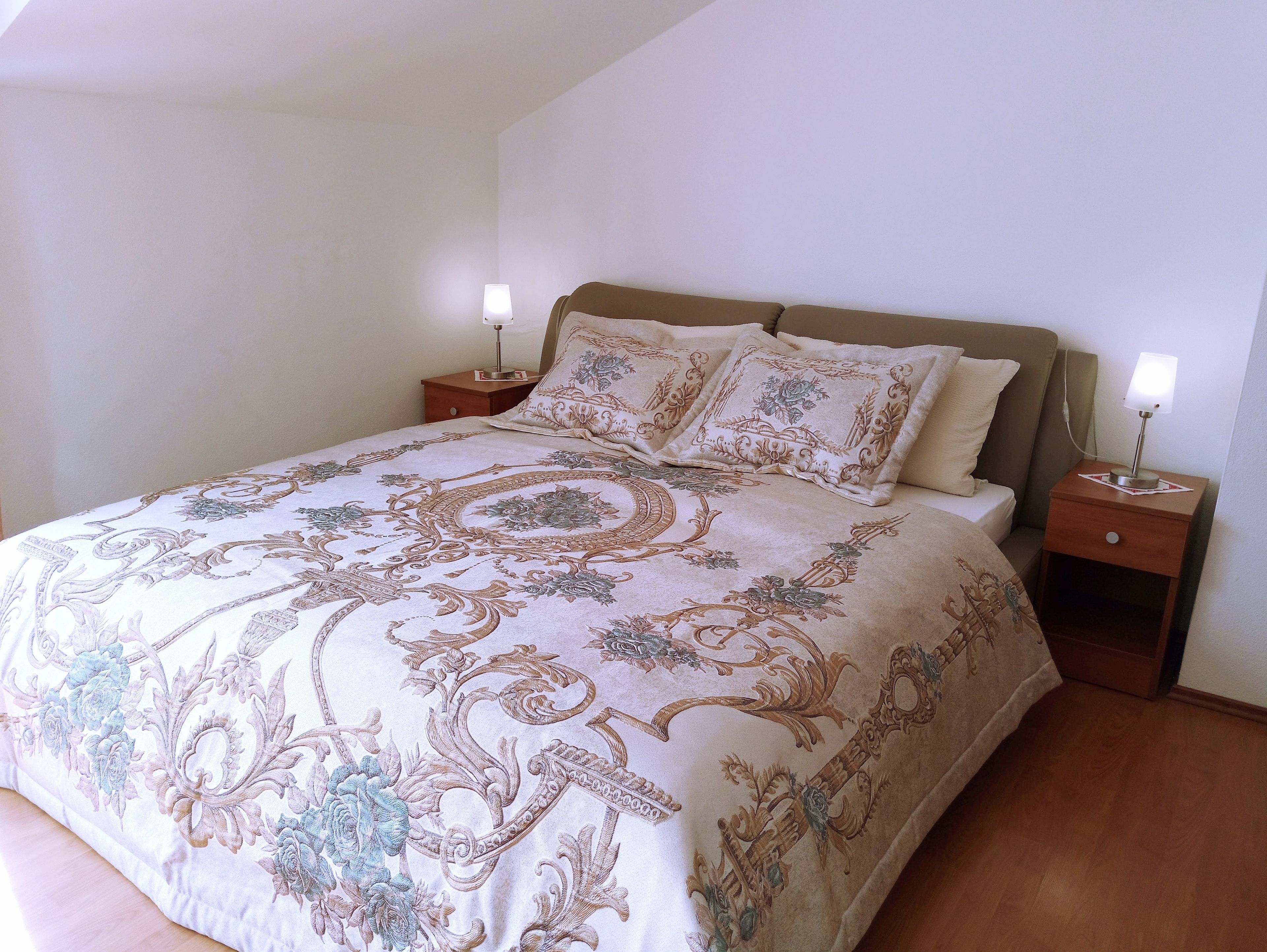 A neatly made bed with a patterned bedspread, two bedside tables with lamps, and a wooden headboard.