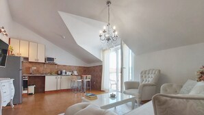 Una sala de estar moderna con sofá, una mesa de centro y un comedor con sillas. Se observa una cocina con armarios y un microondas.