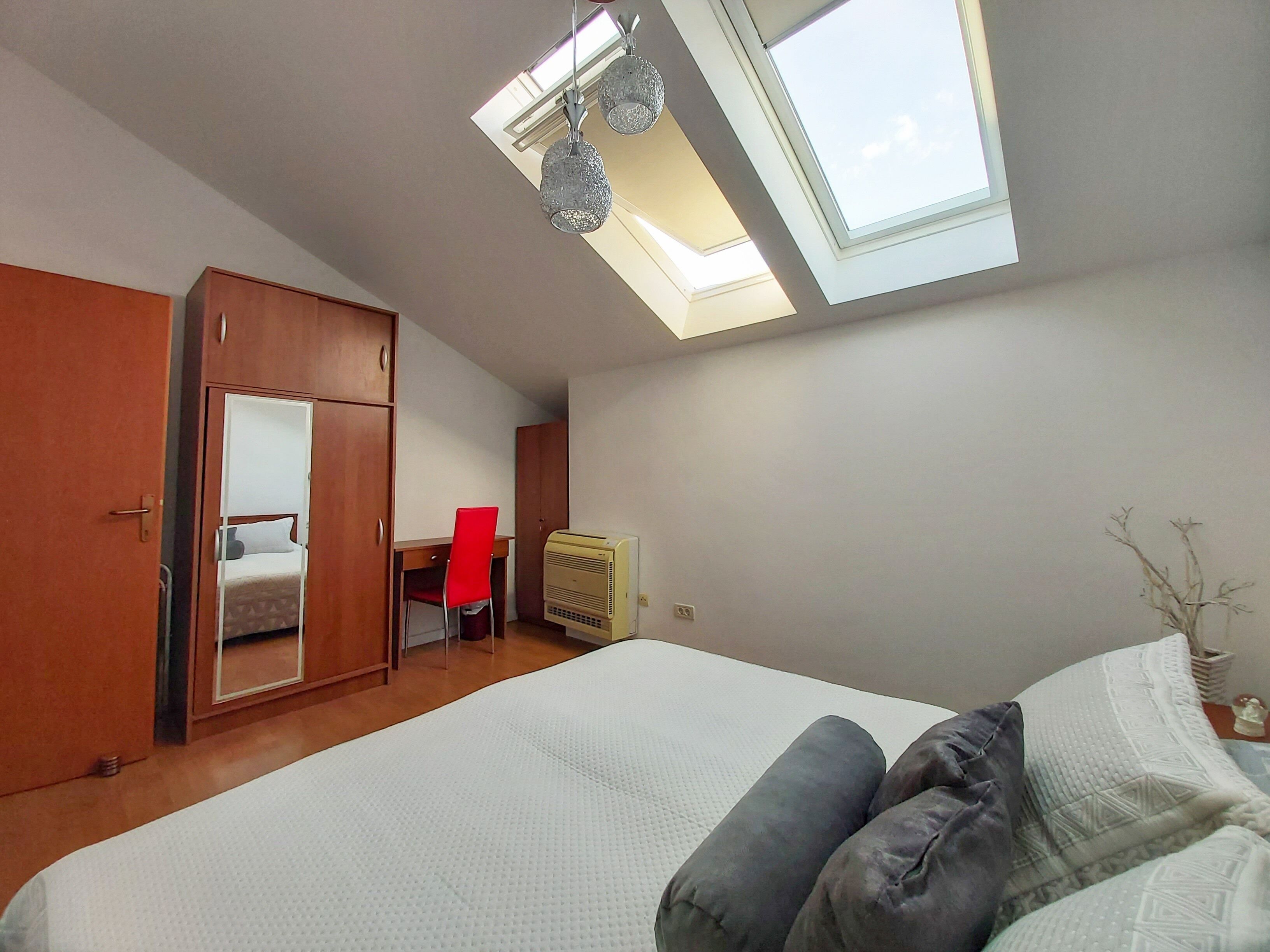 Un dormitorio con tragaluz, cama, armario, escritorio y silla.