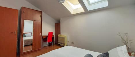 Un dormitorio con tragaluz, cama, armario, escritorio y silla.