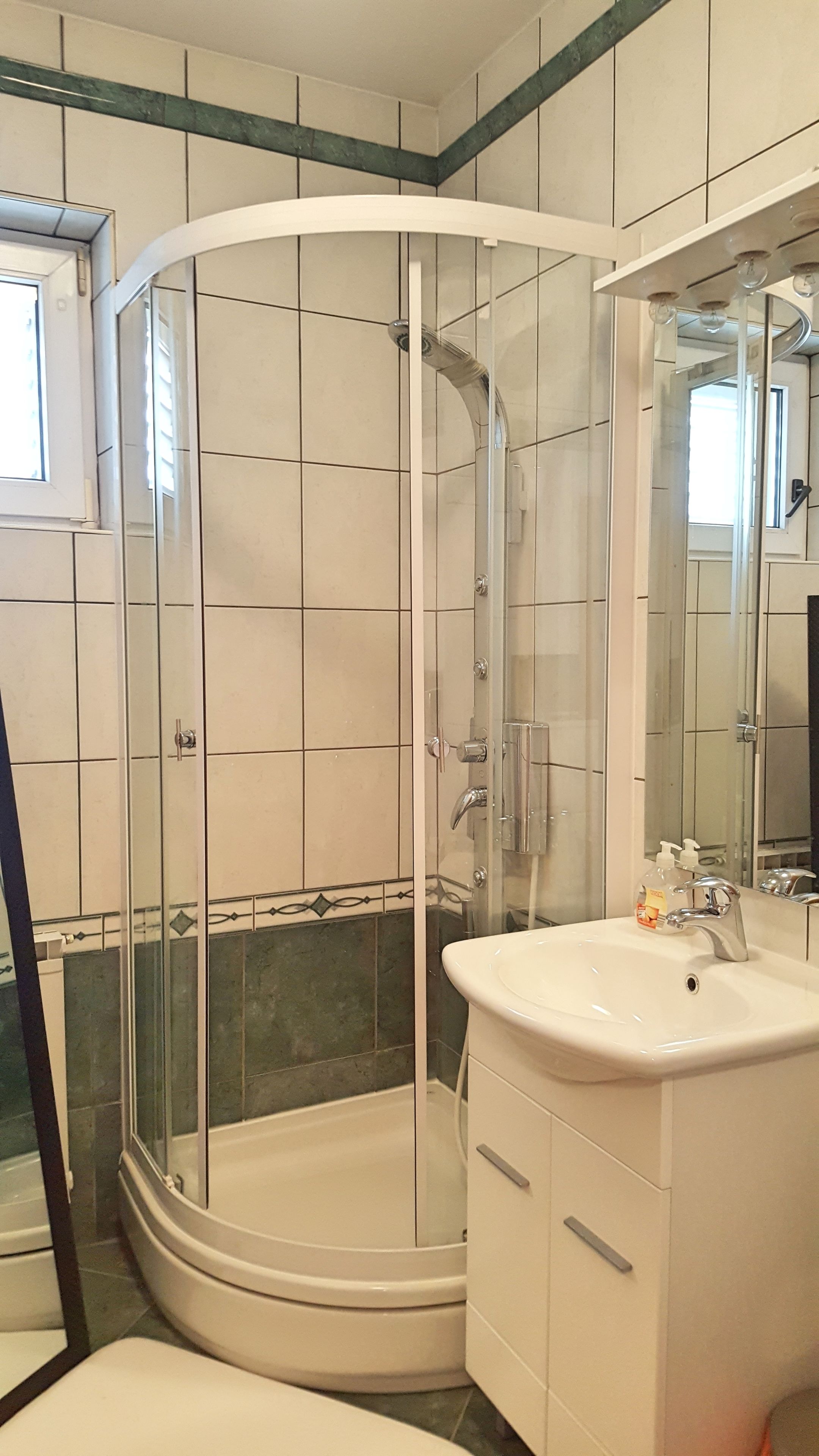 A corner bathroom with a glass-enclosed shower, a white sink, and a mirror above the sink.