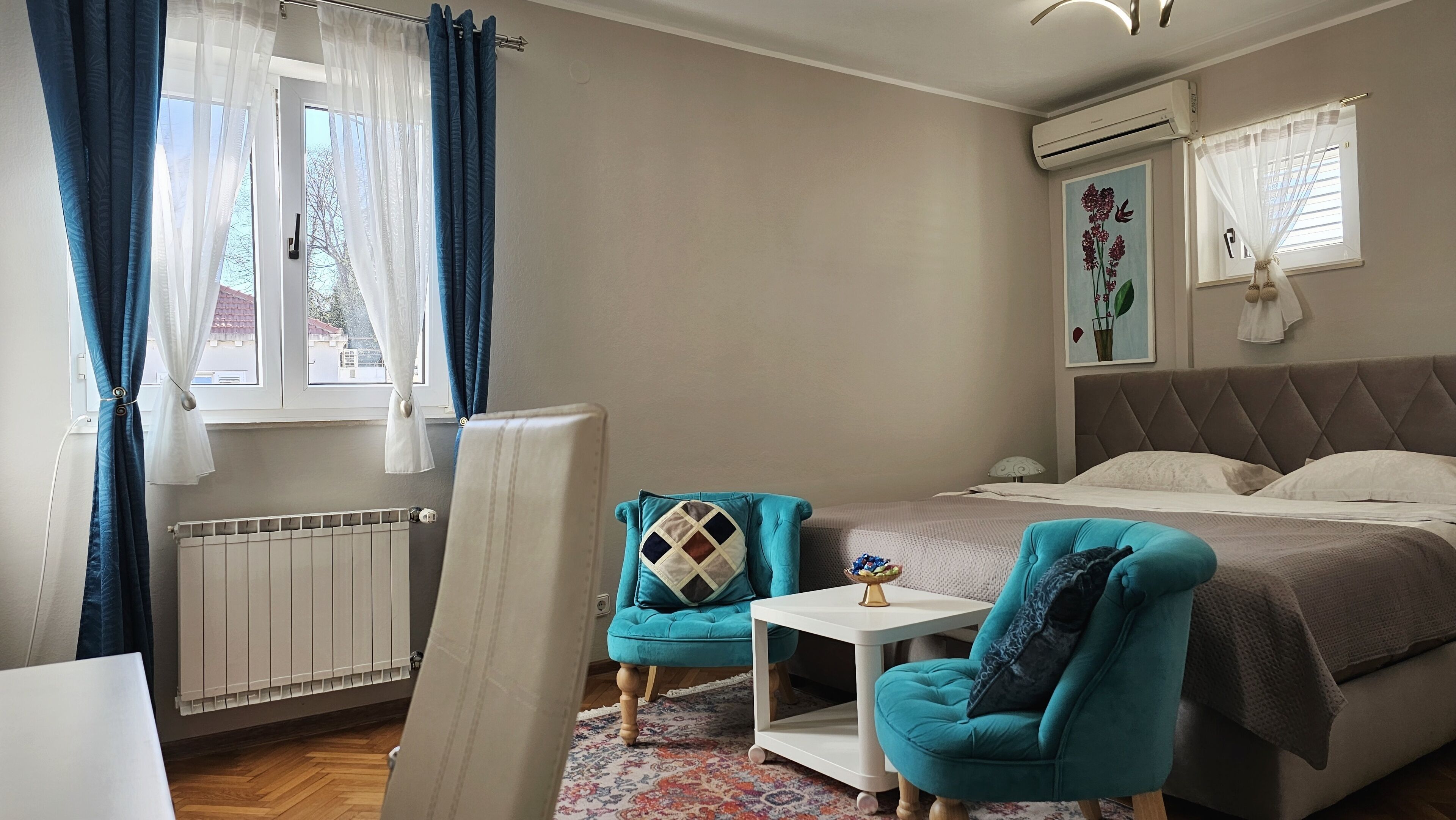 A bedroom with a bed, a chair, a small table, and a radiator.