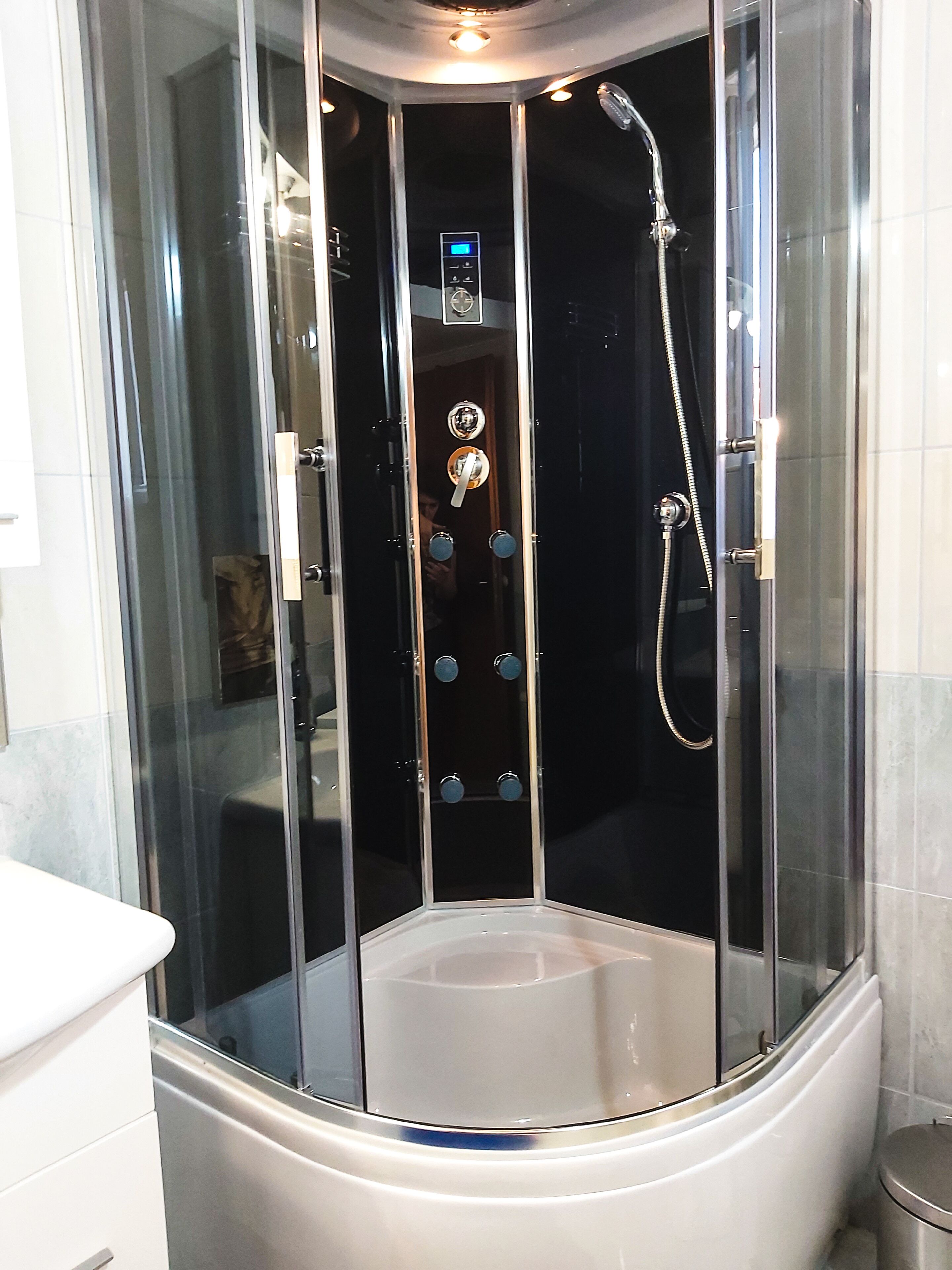 A modern bathroom with a glass-enclosed shower stall, a digital control panel, and a white sink.