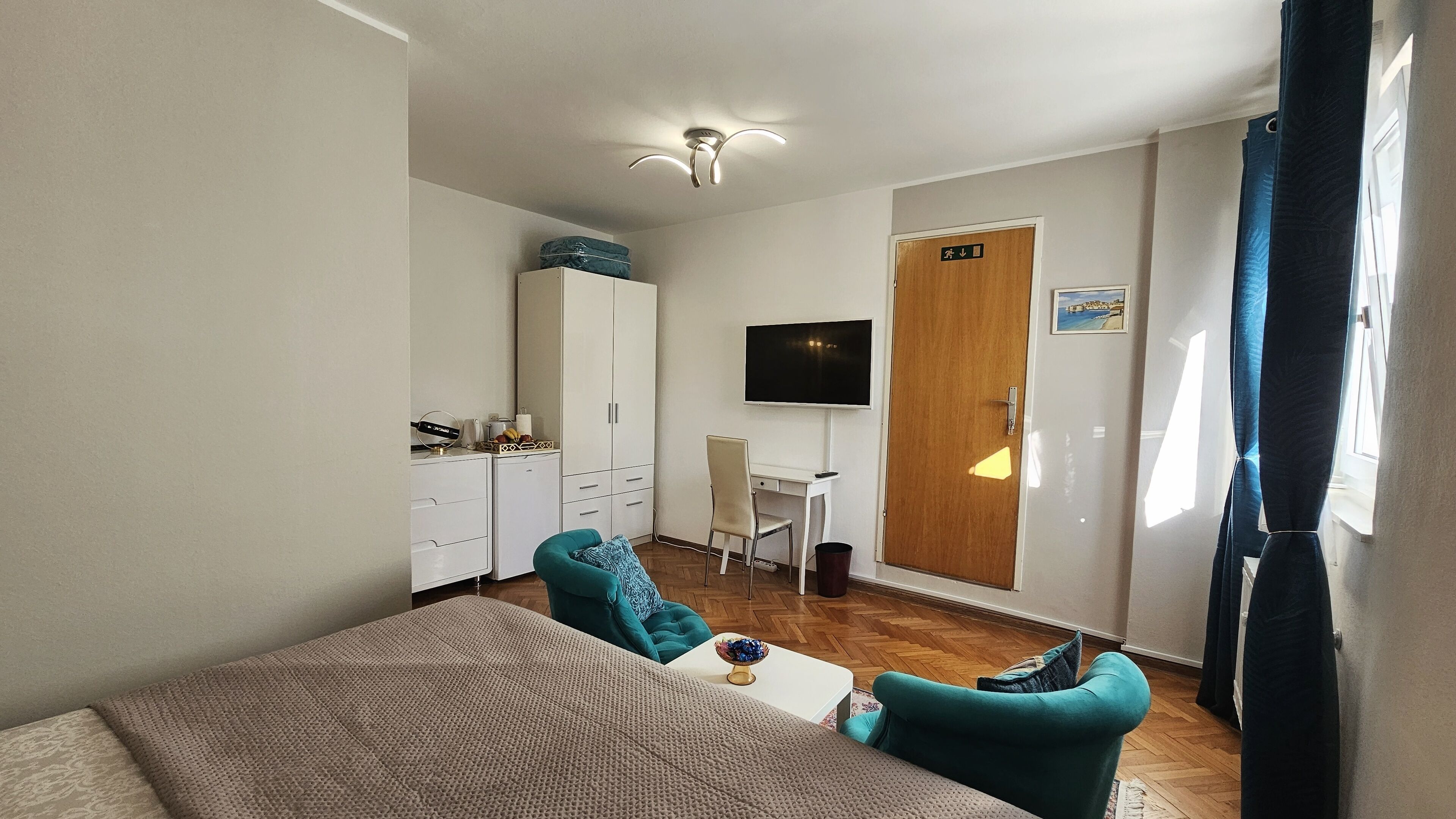 A compact room with a bed, a desk, a chair, a TV, and a wardrobe.