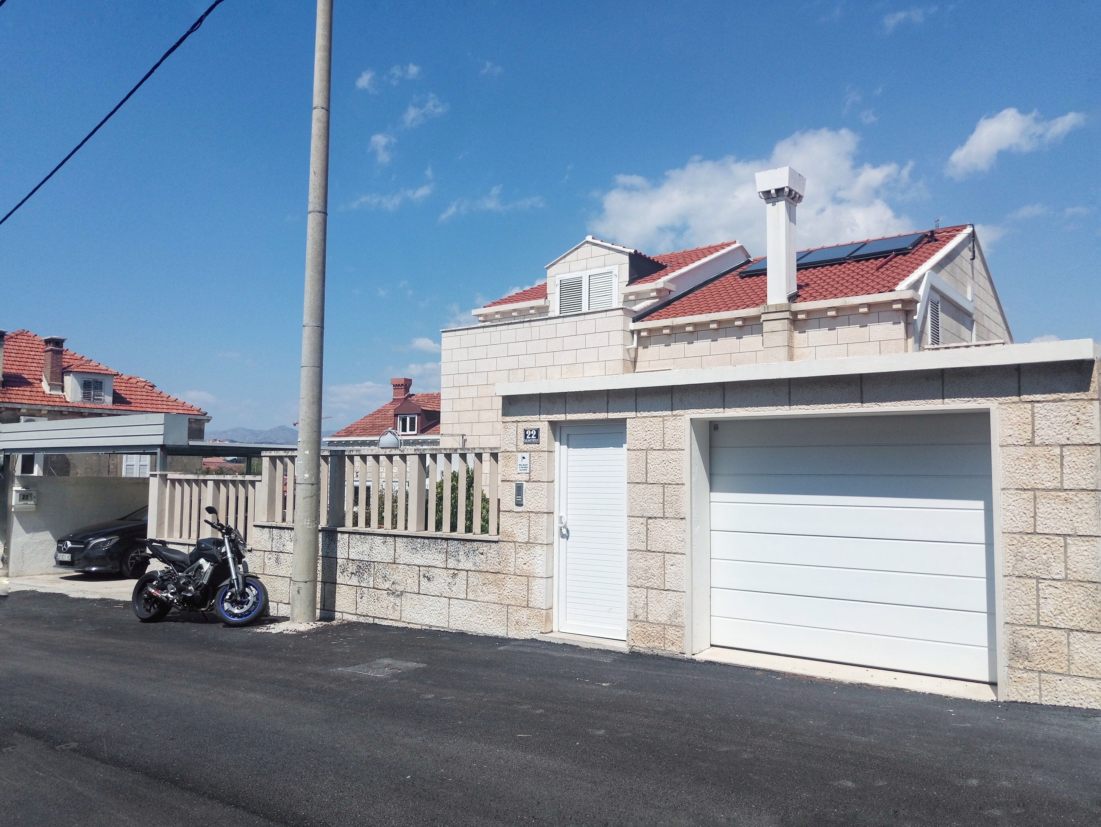 Un edificio residencial con garaje, una motocicleta estacionada afuera y cielo despejado.