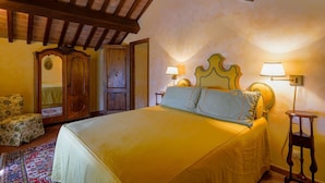 A room with a large bed, wooden ceiling beams, a wooden wardrobe, a chair, and two bedside tables with lamps. - Stunning private villa for 4 guests with A/C, private pool, WIFI, TV, patio and panoramic view (Vicchio)