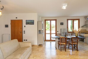 Un salon avec un canapé, un coin repas avec des chaises et une table, une cuisine équipée d’une cuisinière et d’un réfrigérateur, et une porte donnant sur l’extérieur.