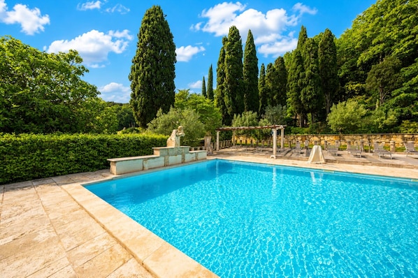 Une piscine rectangulaire à l’eau d’un bleu limpide, entourée d’escaliers en pierre et agrémentée d’une pergola avec des chaises.
