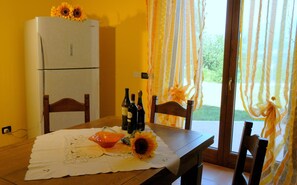 A dining area with a table set for two, a refrigerator, and a window with curtains.