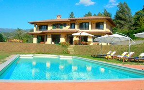 A two-story house with a swimming pool, outdoor seating, and a hillside view.