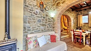 Une pièce chaleureuse avec un mur en pierre, un canapé agrémenté de coussins à motifs floraux, une table à manger avec des chaises et une cheminée.