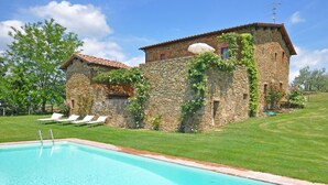 Un bâtiment en pierre doté d’une piscine, de chaises longues blanches et d’une pelouse bien entretenue.
